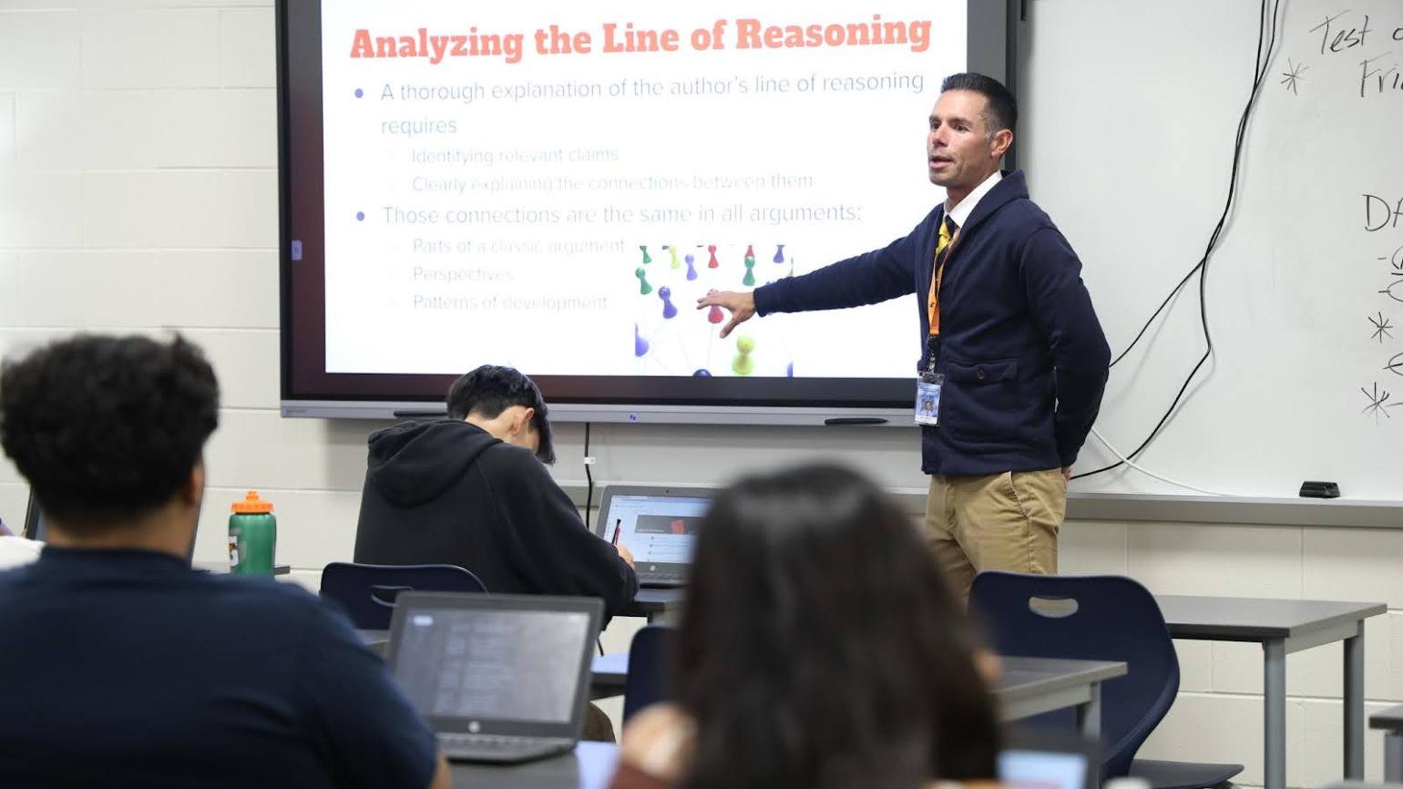 A teacher presents a slide at the front of a classroom.