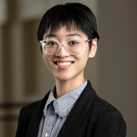 Headshot of Ha Bui, who is pictured wearing white rimmed glasses, a black blazer, and a blue and white striped shirt.