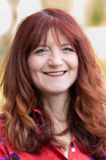Image of smiling woman with shoulder length red hair, wearing a red blouse
