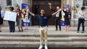 A high school freshman stands in front of his new school with his arms outstretched. School administrators and P-20 partnership staff stand behind him, cheering him on.