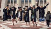Undergraduates in graduation attire jump gleefully in front of Hill Auditorium