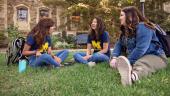 three students sit on the grass, laughing