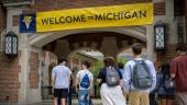 Students at UMSI student orientation walk beneath an arch with a Welcome to Michigan sign above.