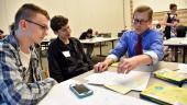 An instructor and two students sitting at a table in a classroom and talk over colored pencil drawings.