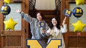 Two people smile and pose with Marsal Education signs in the shape of a heart and text bubble, surrounded by maize and blue balloons, under a Marsal Family School of Education banner.