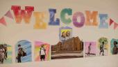 The word “Welcome” is written in large, colorful, cutout letters on a wall of an elementary school. Photos of the students with colorful backgrounds appear under the welcome sign.