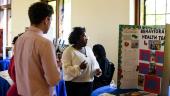 A high school student and a teacher look at the student’s project poster. The poster says 'Behavioral Health.'
