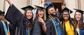 Five new graduates in commencement attire smile and pose for a photo in front of Hill Auditorium